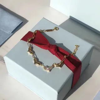 Pulseira de corrente dourada com eslabões em forma de coração vermelha