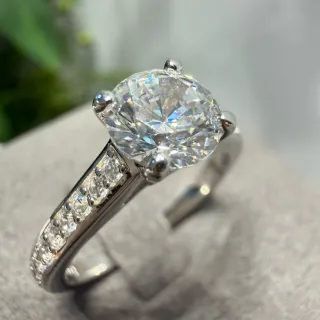 Anillo con piedra central redonda brillante, cuatro garras Pavé y diamantes laterales